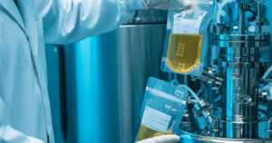 Scientist holding two 100 mL bags of yellow liquid in a bioreactor setup.