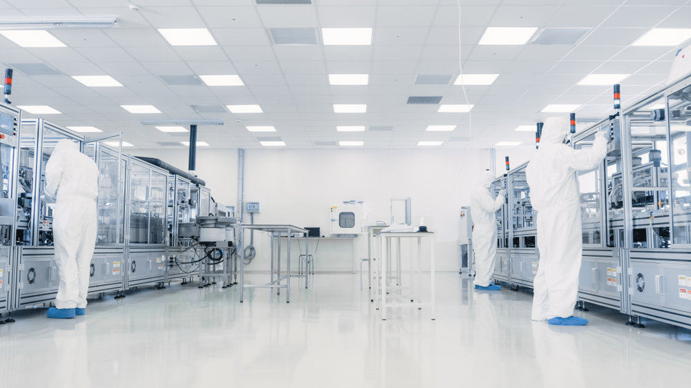 Technicians in cleanroom suits working with advanced manufacturing equipment in a sterile facility.