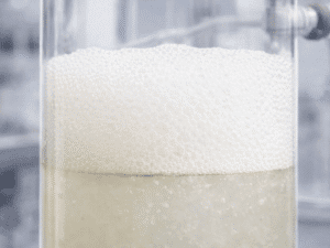 Thick, persistent foam layer at the gas–liquid interface in a transparent vessel, illustrating unusually stable foam formation during processing.